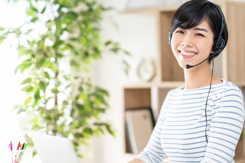 観葉植物のある部屋でヘッドセットを着けてパソコンに向かう女性