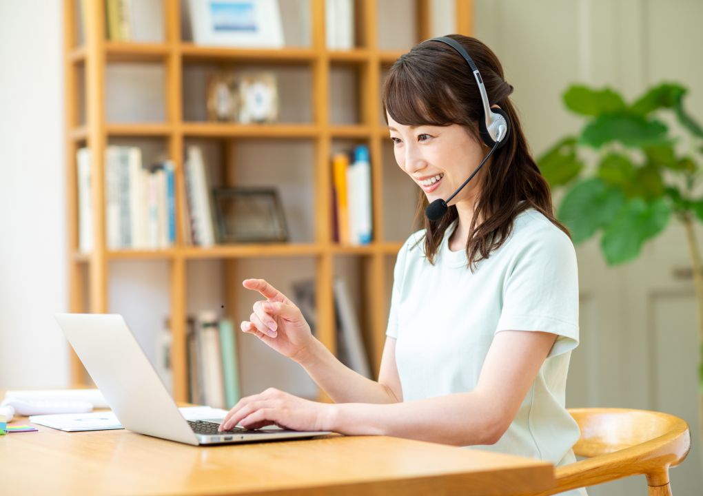 本棚と観葉植物のある部屋でヘッドセットを着けて対応する女性